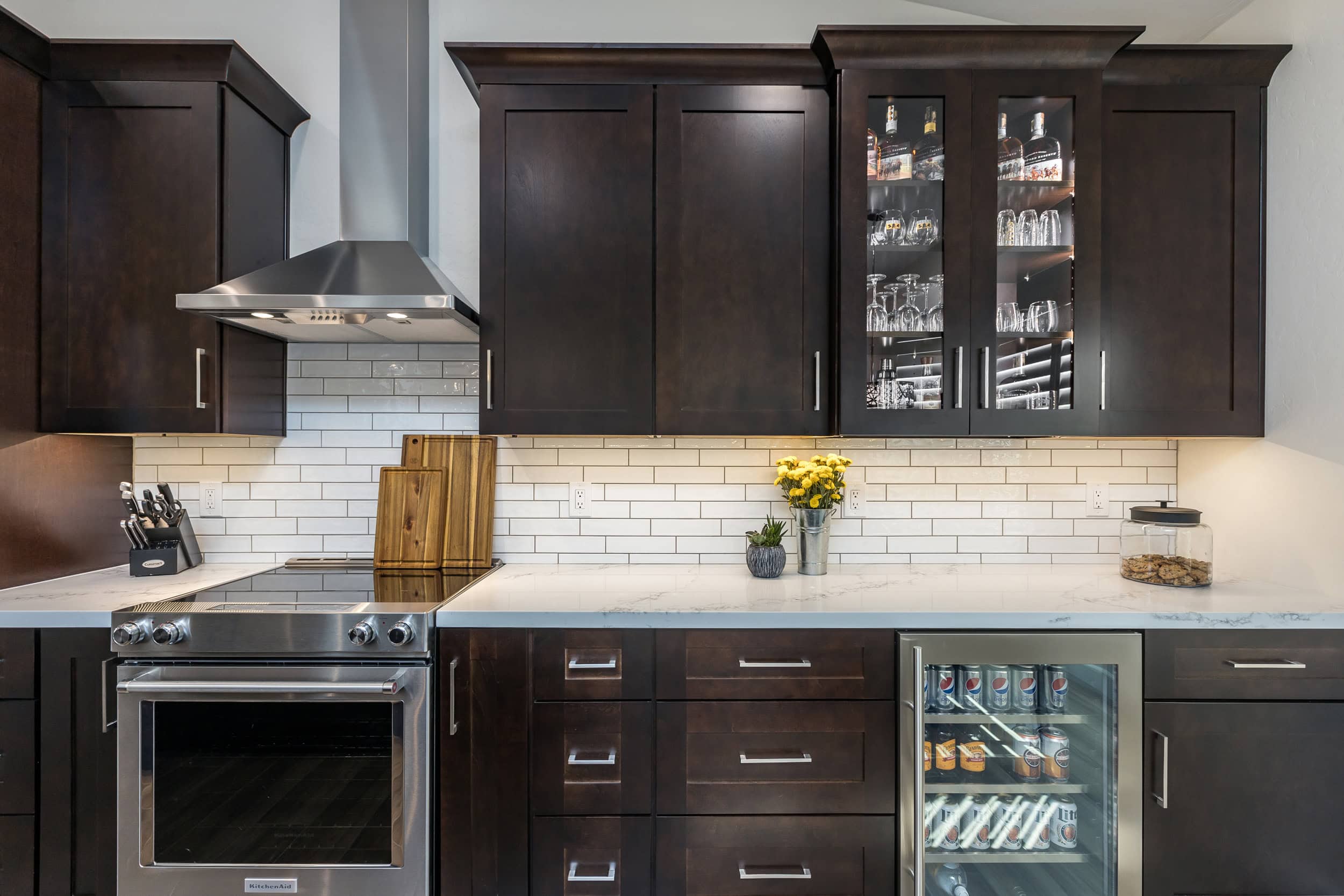 7 beverage area close up Elegant dark wood kitchen cabinets with stainless steel appliances and white subway tile backsplash.